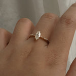 A delicate hand-carved one of a kind "Ilona" style engagement ring by Laurie Fleming Jewellery. The Ring features a 0.5ct marquise cut diamond, a tapered knife-edge band, and small diamond accents on the band shoulders.  The ring is worn on a hand posed in front of some draped gossamer silk fabric.