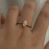 A delicate hand-carved one of a kind "Ilona" style engagement ring by Laurie Fleming Jewellery. The Ring features a 0.5ct marquise cut diamond, a tapered knife-edge band, and small diamond accents on the band shoulders. The ring is worn on a hand posed in front of some draped gossamer silk fabric.