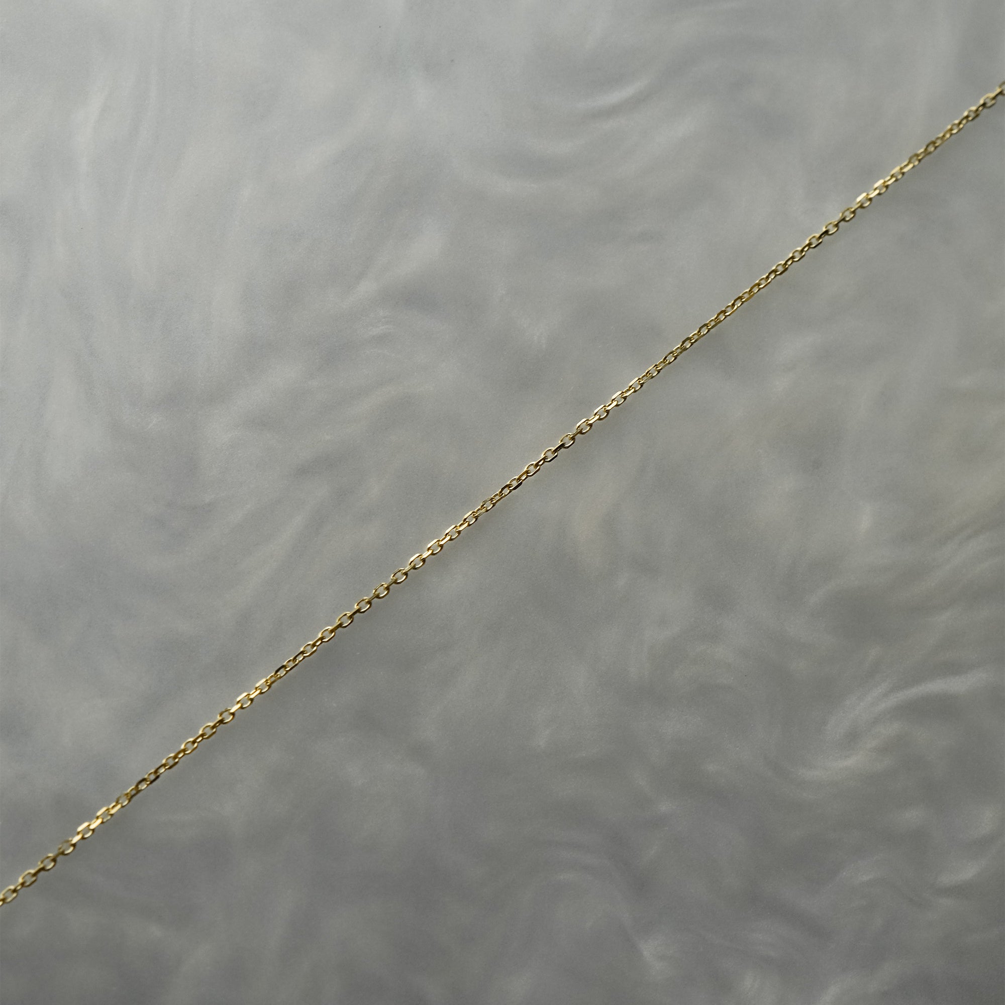 0.68mm super fine and delicate diamond-cut cable chain necklace for charms or pendants. The chain is against a grey background with swirling patterns.