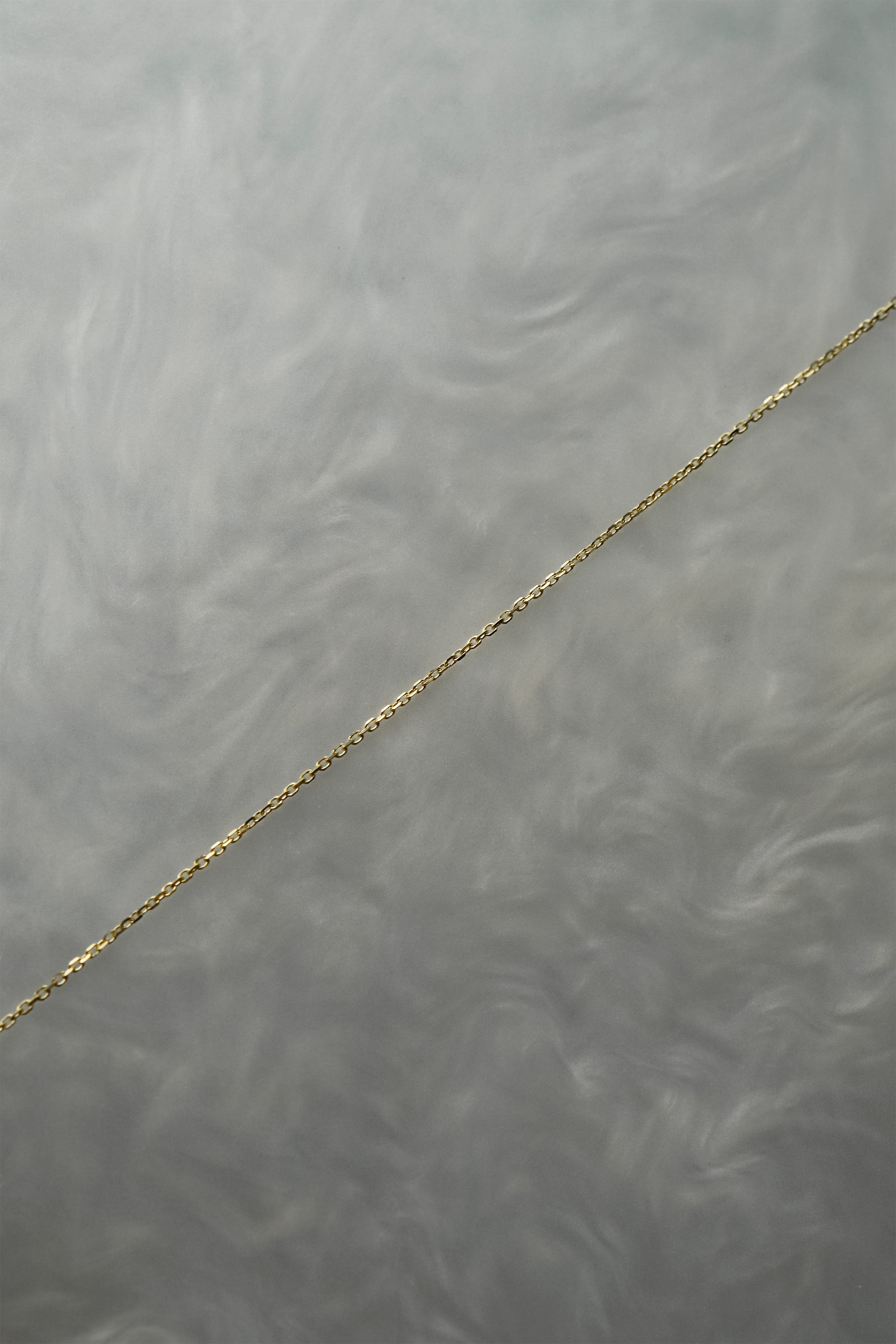 0.68mm super fine and delicate diamond-cut cable chain necklace for charms or pendants. The chain is against a grey background with swirling patterns.