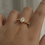 A one of a kind "Daphne" style engagement ring by Laurie Fleming jewellery, featuring a 0.70ct modified oval cut diamond with a unique glimmering sparkle, with diamond clusters on the band. The ring is worn on a hand that is posed in front of some draped gossamer silk fabric.