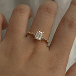 A delicate and ethereal hand-carved one of a kind "Daphne" style engagement ring by Laurie Fleming Jewellery. The ring features a 1.01ct emerald cut diamond with rose and brilliant cut diamond accents on the band in 14k yellow gold. The ring is worn on a hand posed in front of some draped gossamer silk fabric.