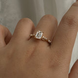 A delicate and ethereal hand-carved one of a kind "Daphne" style engagement ring by Laurie Fleming Jewellery. The ring features a 1.01ct emerald cut diamond with rose and brilliant cut diamond accents on the band in 14k yellow gold. The ring is worn on a hand posed in front of some draped gossamer silk fabric.