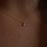 A close up shot of the blue-green teal sapphire Moondew pendant necklace by Laurie Fleming Jewellery in yellow gold, modelled on dark brown skin.