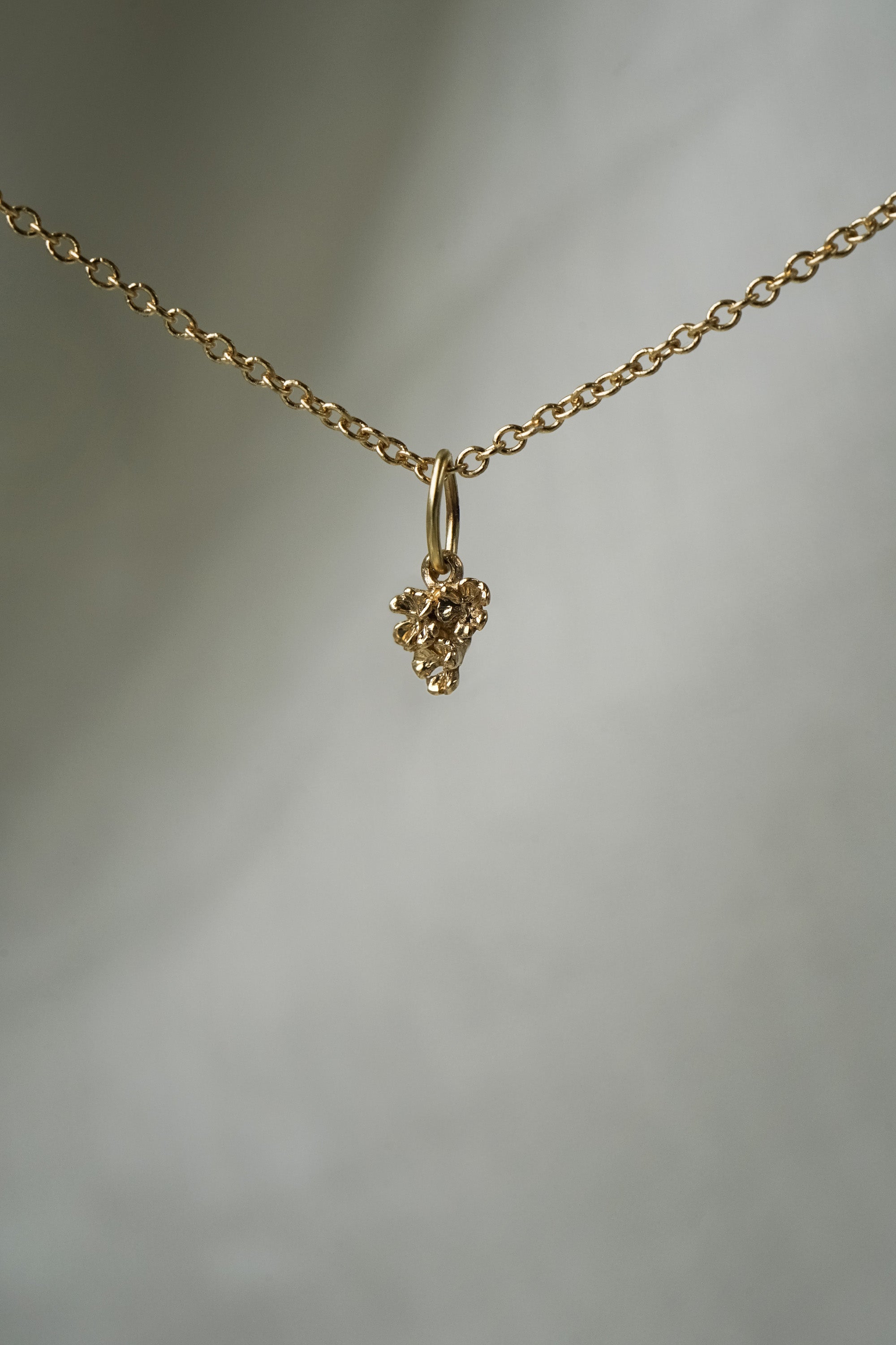A miniature patch of hand-carved clovers, including a lucky four-leaf clover, as a charm, hanging from a 1mm cable chain with smooth oval links. Handmade in Toronto by Laurie Fleming Jewellery.