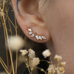 A close up of an ear wearing a Lyrie stud earring with six marquise cut diamonds. There are dried flower stems in the foreground around the ear.