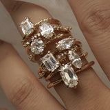 A hand with a stack of diamond engagement rings by Laurie Fleming Jewellery on the middle finger. From top to bottom: Ilona ring with emerald cut diamond, Daphne Ring with oval cut diamond, Ilona ring with round brilliant cut diamond, Aurelia ring with a moval (marquise/oval) diamond, Daphne ring with an emerald cut diamond, Ilona ring with a marquise cut diamond, Aurelia ring with an oval cut diamond.