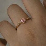 A delicate hand-carved one of a kind "Ilona" style engagement ring by Laurie Fleming Jewellery. The ring features a rose cut pink sapphire centre, a tapered knife-edge band, and small diamond accents on the band shoulders. The ring is worn on a hand against a light grey background.