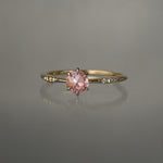 A delicate hand-carved one of a kind "Ilona" style engagement ring by Laurie Fleming Jewellery. The ring features a rose cut pink sapphire centre, a tapered knife-edge band, and small diamond accents on the band shoulders.  The ring is situated against a medium grey background.