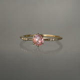 A delicate hand-carved one of a kind "Ilona" style engagement ring by Laurie Fleming Jewellery. The ring features a rose cut pink sapphire centre, a tapered knife-edge band, and small diamond accents on the band shoulders.  The ring is situated against a medium grey background.