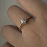 A one of a kind 14k champagne gold "Water Lily" engagement ring by Laurie Fleming Jewellery with a silver-blush colour change Montana sapphire centre held in delicate hand-carved claw prongs. A sprinkling of petite and delicate diamonds dance along the band. The ring is worn on a hand against a light grey background.