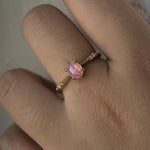 A delicate hand-carved one of a kind "Ilona" style engagement ring by Laurie Fleming Jewellery. The ring features a silky and opalescent rose cut oval pink sapphire centre, a tapered knife-edge band, and small diamond accents on the band shoulders. The ring is worn on a hand against a light grey background.