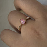 A delicate hand-carved one of a kind "Ilona" style engagement ring by Laurie Fleming Jewellery. The ring features a silky and opalescent rose cut oval pink sapphire centre, a tapered knife-edge band, and small diamond accents on the band shoulders. The ring is worn on a hand against a light grey background.