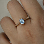 A delicate hand-carved one of a kind "Ilona" style engagement ring by Laurie Fleming Jewellery. The ring features a 0.93ct geometric oval cut silky periwinkle blue sapphire centre, a tapered knife-edge band, and small diamond accents on the band shoulders.  The ring is worn on a hand against a plain light grey background.