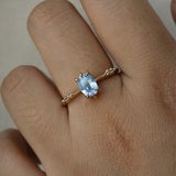 A delicate hand-carved one of a kind "Ilona" style engagement ring by Laurie Fleming Jewellery. The ring features a 0.93ct geometric oval cut silky periwinkle blue sapphire centre, a tapered knife-edge band, and small diamond accents on the band shoulders.  The ring is worn on a hand against a plain light grey background.