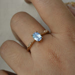 A delicate hand-carved one of a kind "Ilona" style engagement ring by Laurie Fleming Jewellery. The ring features a 0.93ct geometric oval cut silky periwinkle blue sapphire centre, a tapered knife-edge band, and small diamond accents on the band shoulders.  The ring is worn on a hand against a plain light grey background.