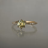 An elegant, one of a kind "Ilona" style engagement ring by Laurie Fleming Jewellery. The ring features a 1ct round brilliant cut yellow-grey Montana sapphire poised atop a tapered knife-edge band with small diamond accents on the band shoulders.  The ring is situated against a medium grey background.