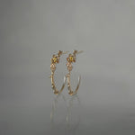 A pair of Laurie Fleming Jewellery "Large Buttercup Hoop" earrings, featuring petite hand-carved buttercup flowers with a yellow sapphire centre. The earrings are on a medium grey background.