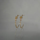 A pair of Laurie Fleming Jewellery "Large Buttercup Hoop" earrings, featuring petite hand-carved buttercup flowers with a yellow sapphire centre. The earrings are on a medium grey background.