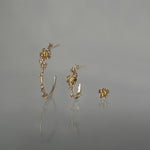 A line-up of three Laurie Fleming Jewellery earrings over a medium grey background. On the left, a large buttercup hoop. In the middle,  a small buttercup hoop. On the right, a buttercup stud earring. All three earrings feature hand-carved petite buttercup flower blossoms with yellow sapphire centres.