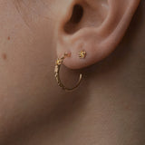 Close up of an ear wearing two Laurie Fleming Jewellery earrings; the first hole has a Large Buttercup Hoop, and the second hole has a Buttercup stud. Both earrings feature hand-carved buttercup flowers and yellow sapphires.