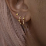 A close up of an ear wearing three Laurie Fleming Jewellery earrings. In the first hole, a large buttercup hoop. The second hole has a small buttercup hoop. The third hole has a buttercup earring. All three earrings feature hand-carved petite buttercup flower blossoms with yellow sapphire centres.