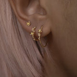 A close up of an ear wearing three Laurie Fleming Jewellery earrings. In the first hole, a large buttercup hoop. The second hole has a small buttercup hoop. The third hole has a buttercup earring. All three earrings feature hand-carved petite buttercup flower blossoms with yellow sapphire centres.