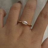 A one of a kind "Aurelia" style engagement ring by Laurie Fleming Jewellery, featuring a unique "moval" (marquise/oval hybrid) cut diamond set East-West, on a gently tapered and rounded solid gold band. The ring is worn on a hand that is posed in front of some draped gossamer silk fabric.