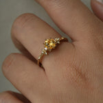 A hand wearing a one of a kind 18k yellow gold Water Lily engagement ring with a bright yellow round Montana sapphire centre with clusters of diamonds on the band.