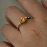A hand wearing a one of a kind 18k yellow gold Water Lily engagement ring with a bright yellow round Montana sapphire centre with clusters of diamonds on the band.