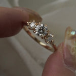 Round Brilliant Cut Three-stone diamond Wild Iris engagement ring by Laurie Fleming Jewellery, held between two fingers and rotated from side to side.
