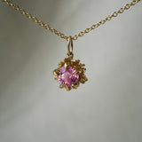 A hand-carved primrose flower charm with a 5mm pink sapphire at its centre, hanging from a 1mm cable chain with smooth oval links. Handmade in Toronto by Laurie Fleming Jewellery.