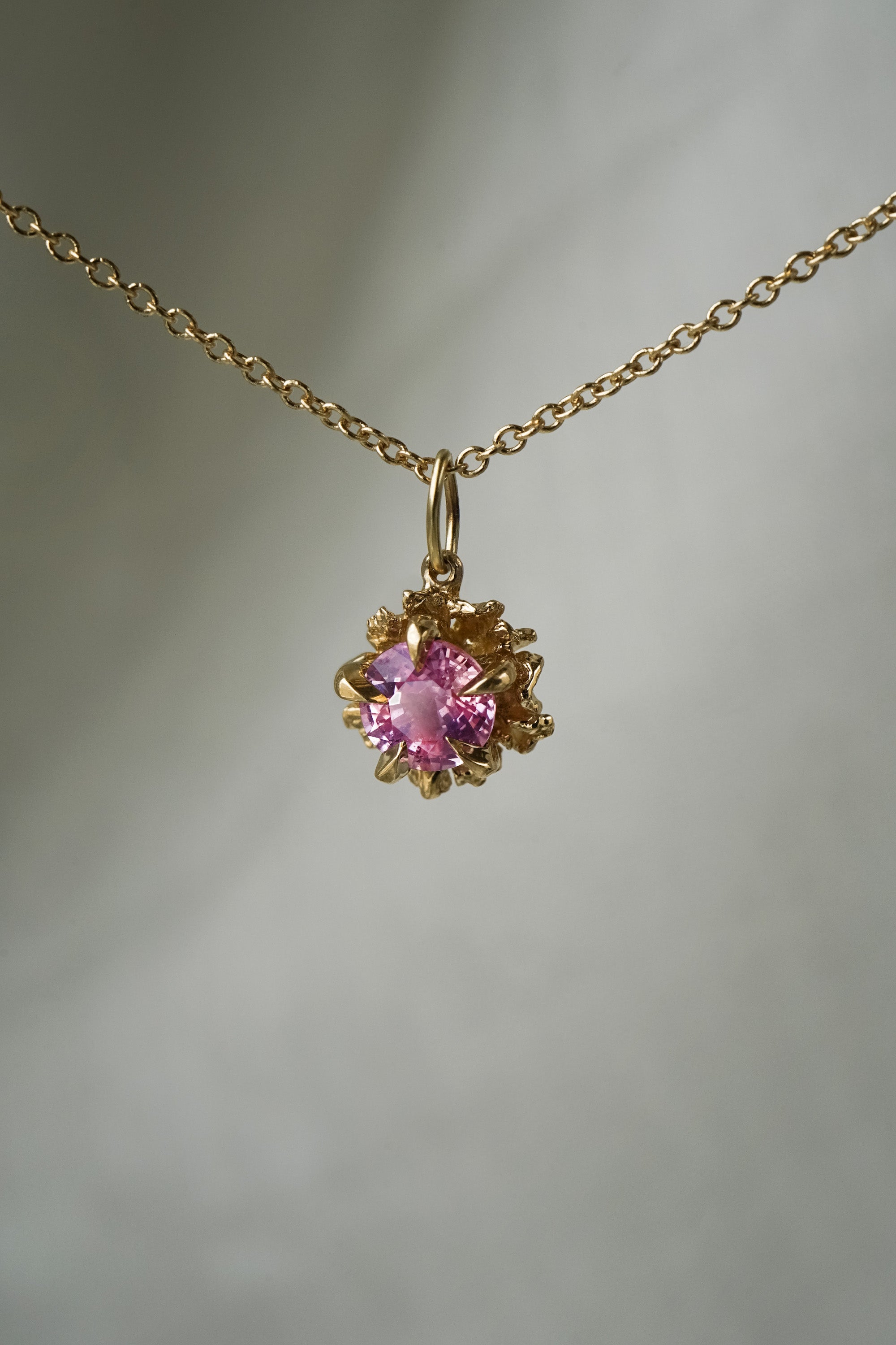 A hand-carved primrose flower charm with a 5mm pink sapphire at its centre, hanging from a 1mm cable chain with smooth oval links. Handmade in Toronto by Laurie Fleming Jewellery.