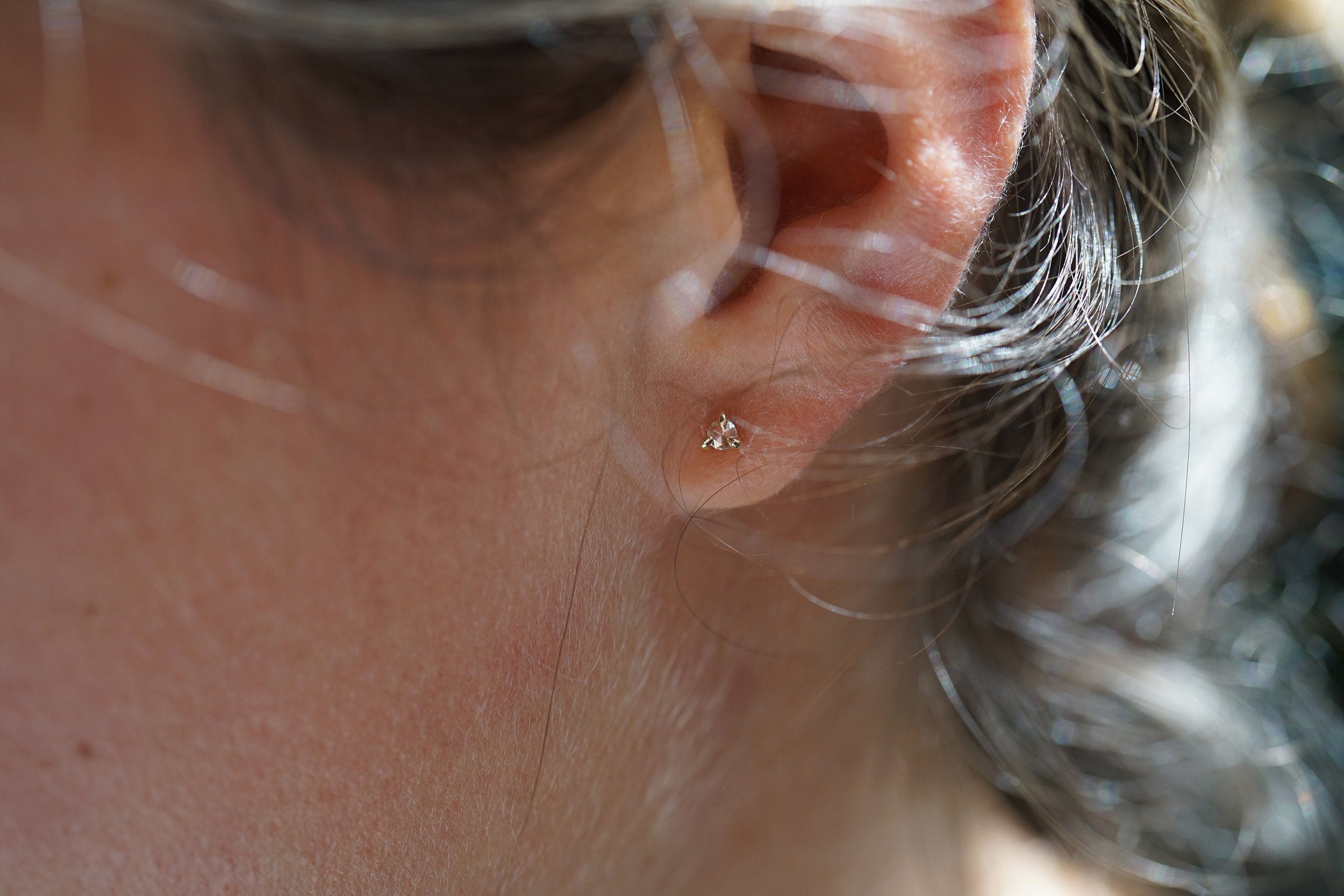 A close up of an ear wearing a Selene Stud earring by Laurie Fleming Jewellery, which features a rose cut diamond held in three delicate claw-shaped prongs.
