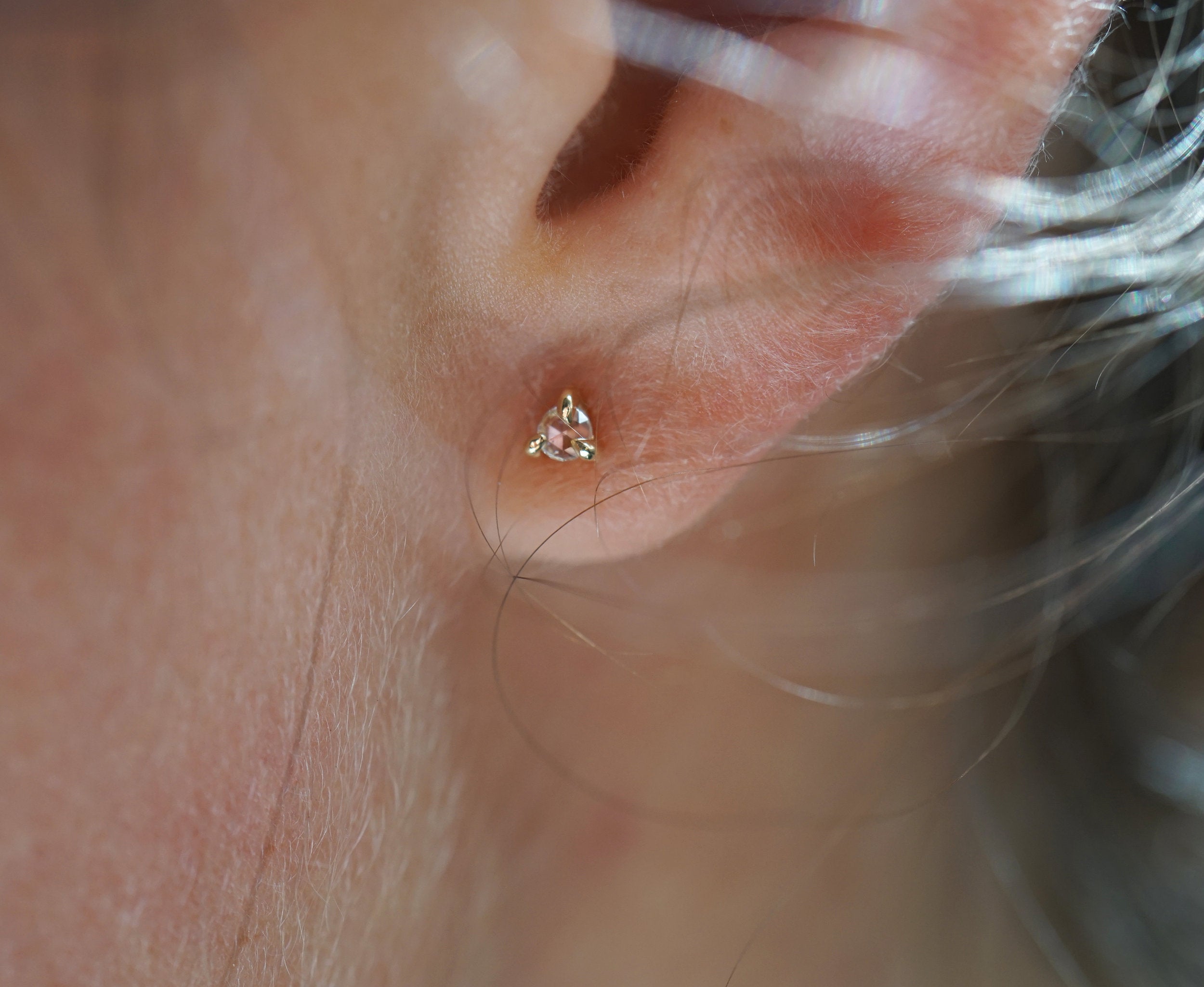 A close up of an ear wearing a Selene Stud earring by Laurie Fleming Jewellery, which features a rose cut diamond held in three delicate claw-shaped prongs.