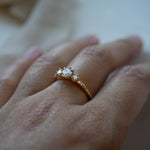 A Wild Iris three stone Engagement Ring by Laurie Fleming Jewellery, worn on a hand. The angle shows the side view of the ring, including its smooth solid gold band and its flat, plain sides which let it stack beautifully with other rings.