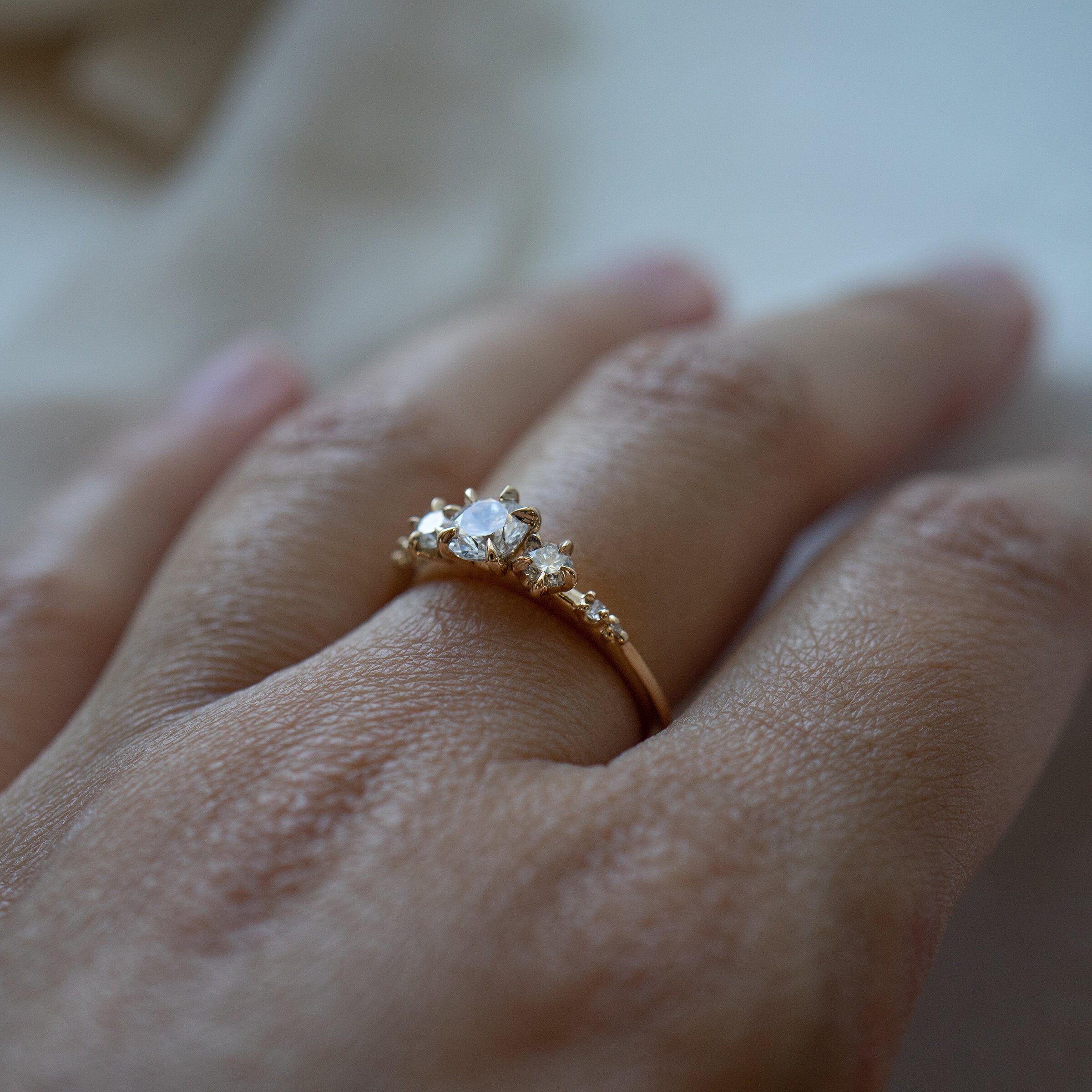 A Wild Iris three stone Engagement Ring by Laurie Fleming Jewellery, worn on a hand. The angle shows the side view of the ring, including its smooth solid gold band and its flat, plain sides which let it stack beautifully with other rings.