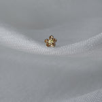 A single Buttercup Stud by Laurie Fleming Jewellery resting on loosely woven white silk. The earring features a hand-carved buttercup flower with a yellow sapphire centre.