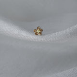 A single Buttercup Stud by Laurie Fleming Jewellery resting on loosely woven white silk. The earring features a hand-carved buttercup flower with a yellow sapphire centre.