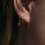 A close-up of an ear wearing three Laurie Fleming Jewellery earrings. In the first hole, a small buttercup hoop featuring handcarved buttercup flowers with a yellow sapphire centre. In the second hole, a Calla Lily earring, with a delicately hand-carved petite calla lily flower with a stem wrapping around the lobe. In the third hole, the tiniest hidden fairy stud with two delicate golden wings over a sparkling diamond.