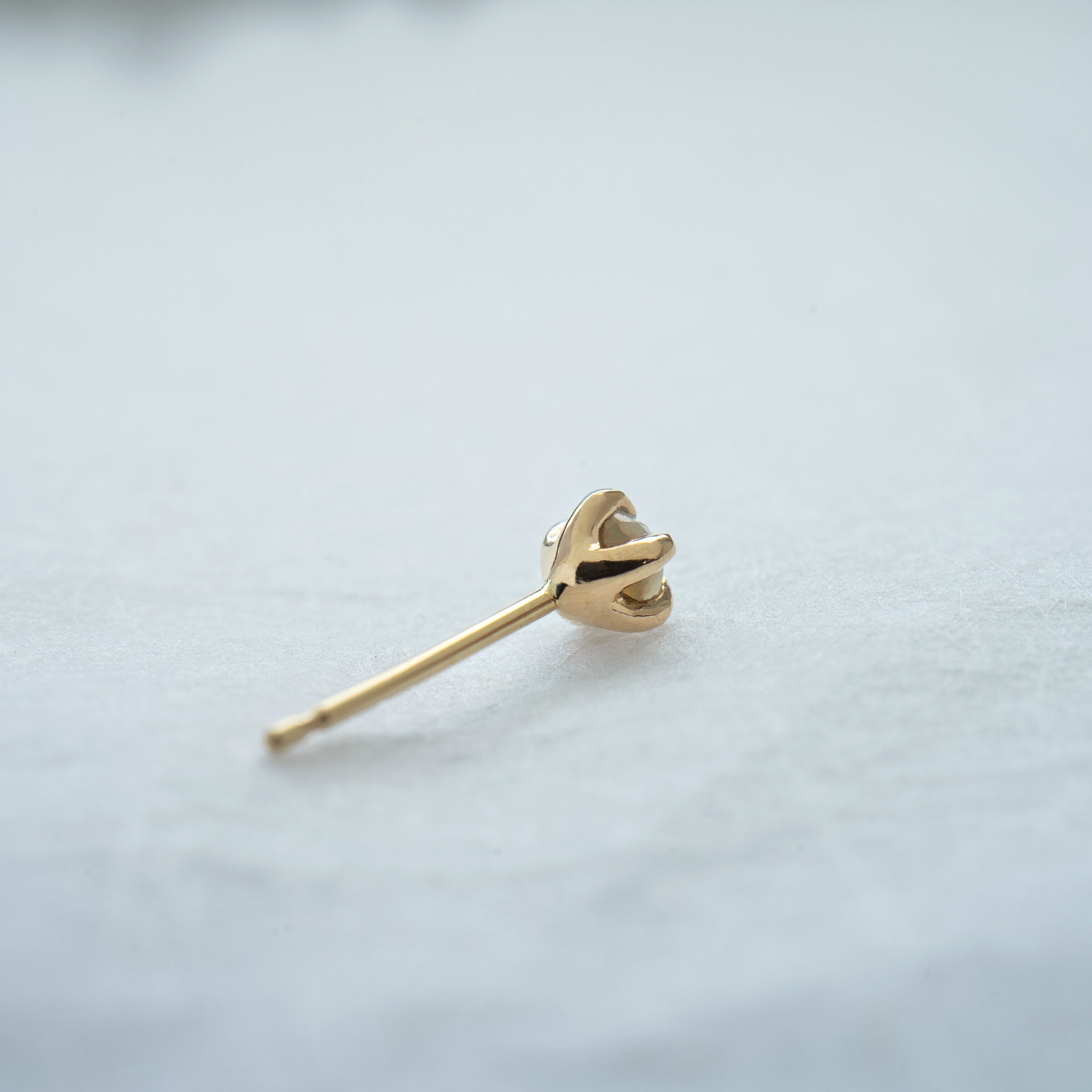 A photo showing the back of a Moondew stud earring, showing its delicately carved basket holding the stone in five claw shaped prongs.