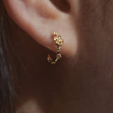 Close-up of an ear wearing a Laurie Fleming Jewellery "Small Buttercup Hoop" earring, featuring petite hand-carved buttercup flowers with a yellow sapphire centre.