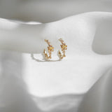 A pair of Laurie Fleming Jewellery "Small Buttercup Hoop" earrings, featuring petite hand-carved buttercup flowers with a yellow sapphire centre. The earrings are displayed against rippling smooth white fabric.