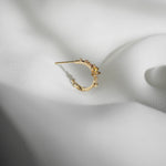 A single Laurie Fleming Jewellery "Small Buttercup Hoop" earring, seen from the side, featuring petite hand-carved buttercup flowers with a yellow sapphire centre. The earring is displayed against rippling smooth white fabric.
