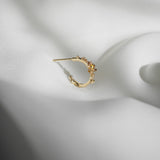 A single Laurie Fleming Jewellery "Small Buttercup Hoop" earring, seen from the side, featuring petite hand-carved buttercup flowers with a yellow sapphire centre. The earring is displayed against rippling smooth white fabric.
