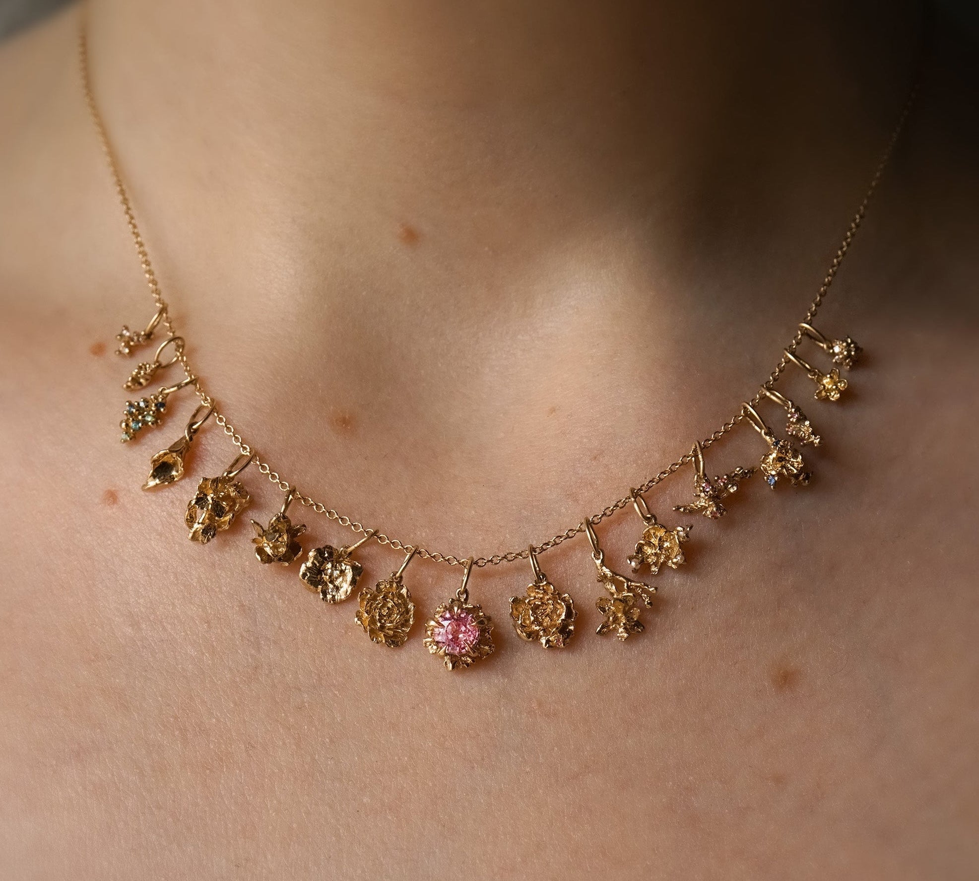 A close-up of a neck wearing a fine, 16 inch cable chain. On the chain are 17 handmade flower charms in solid gold with natural diamonds and sapphires, by Laurie Fleming Jewellery.