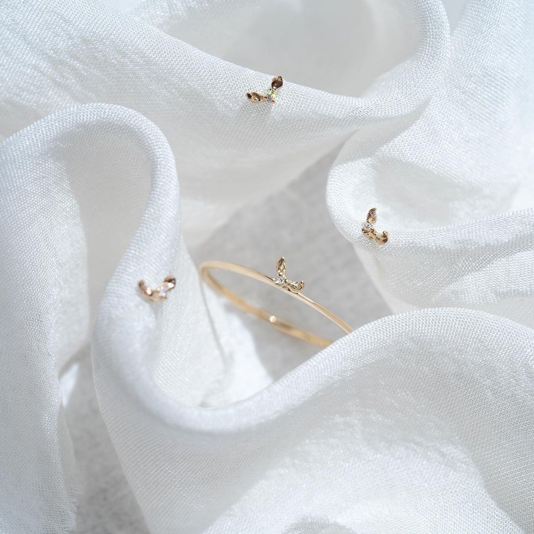 Ripples of white silk fill the frame. Nestled at the centre, a Hidden Fairy Ring by Laurie Fleming Jewellery. Scattered around are three Hidden Fairy Stud earrings.