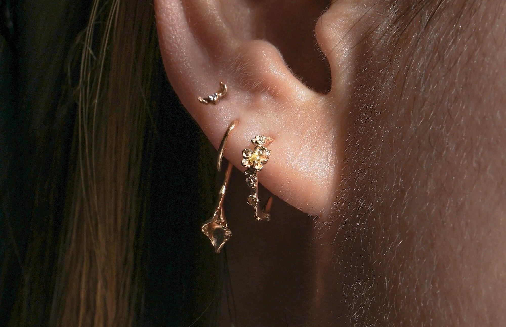 Close up of an ear wearing three Laurie Fleming Jewellery Earrings. From left to right: Hidden Fairy Stud, Calla Lily Earring, Small Buttercup Hoop with Yellow Sapphire