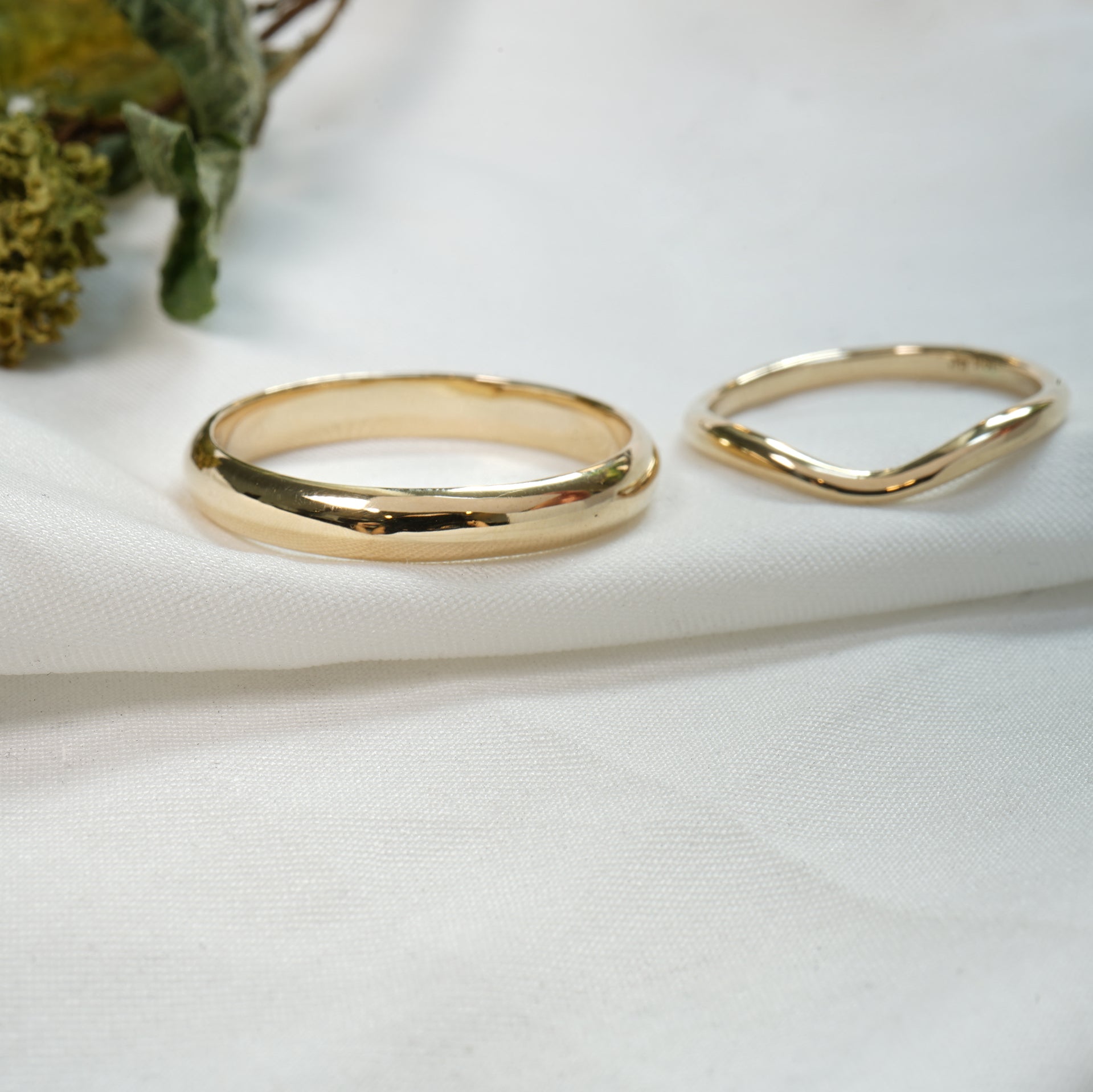 Two solid 14k gold Laurie Fleming rings sitting side-by-side on white fabric. Left to right: 3.5mm half round Oak Band, Undine Curved Band