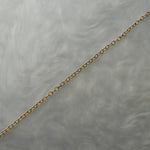 1.4mm cable chain with smooth oval links in solid 14k gold, perfect for wearing on its own or with charms or pendants. The chain is against a grey background with swirling patterns.